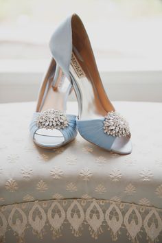 a pair of blue high heeled shoes sitting on top of a white ottoman next to a window