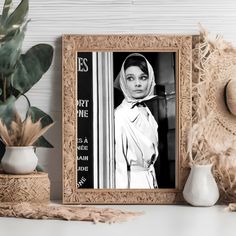 a black and white photo of a woman wearing a headscarf next to a potted plant