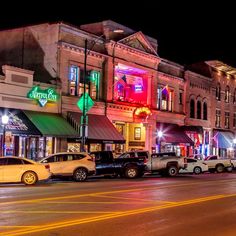 cars are parked on the street in front of buildings at night time with neon lights