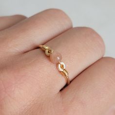 a woman's hand wearing a gold ring with pearls on the band and a knot around it