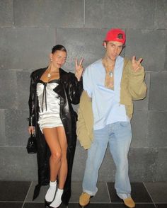 a man and woman standing next to each other in front of a wall with two fingers up