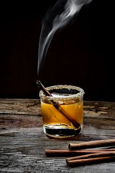 a glass filled with liquid next to two cinnamon sticks on top of a wooden table