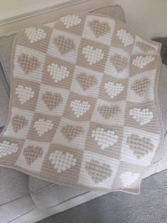 a crocheted blanket with hearts on it sitting on top of a gray couch