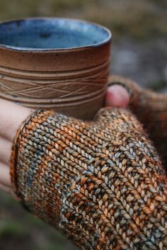 a person's hand holding a brown and blue cup with woven sleeves on it