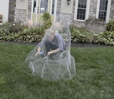 a statue of a woman in a fish net sitting on top of grass next to a house