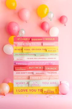 a stack of books sitting on top of a pink table next to balloons and confetti