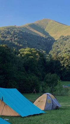 two tents pitched up in the grass with mountains in the background