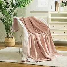 a pink blanket sitting on top of a white chair next to a potted plant