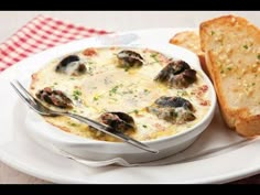 a white plate topped with a bowl of soup next to a slice of bread