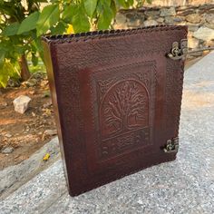 a brown leather journal sitting on top of a stone slab next to a green bush