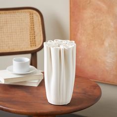 a white vase sitting on top of a table next to a cup and saucer