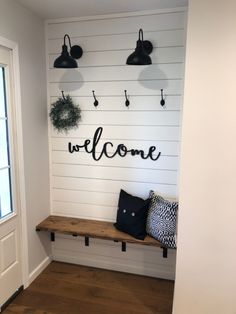 a welcome sign on the wall next to a wooden bench with two black and white pillows