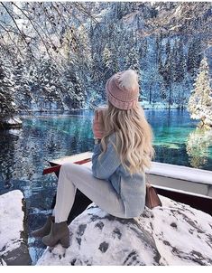 a woman sitting on the edge of a boat looking out over a lake in winter