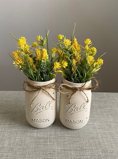 two mason jars with yellow flowers tied to the lids are sitting side by side on a table