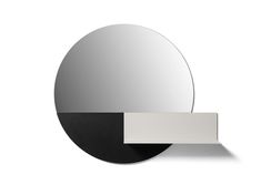 a round mirror sitting on top of a white wall next to a black and white shelf