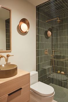 a bathroom with a toilet, sink and shower stall in the background is a green tiled wall