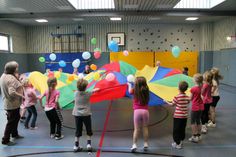 a group of children standing on top of a gym floor holding kites in the air