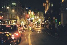 a busy city street at night with cars parked on the side and people walking down the sidewalk