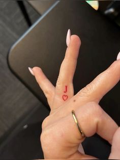 a woman's hand with a small heart tattoo on her thumb and the word love written in red ink