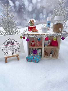 a small doll house in the snow next to a christmas tree and card board with gifts on it