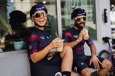 two bicyclists sitting on the side of a building with drinks in their hands