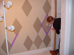 a woman painting a wall with purple tape