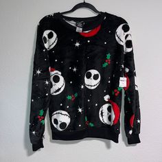 a black sweater with skulls and christmas decorations on it hanging from a hanger in front of a white wall