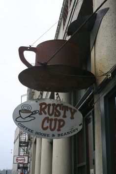 rusty cup coffee house and bakery sign hanging from the side of a building