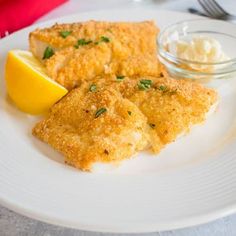 a white plate topped with fried fish next to lemon wedges and cottage cheese sauce