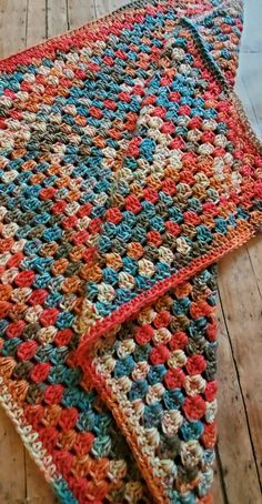 a multicolored crocheted blanket laying on top of a wooden floor