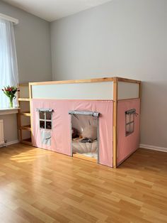 a pink tent with two windows on top of it in a room that has hardwood floors