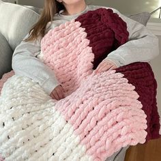 a woman sitting on a couch holding a pink and white crocheted blanket in the shape of a heart