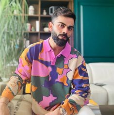 a man sitting on top of a couch wearing a colorful shirt and watch in his hand