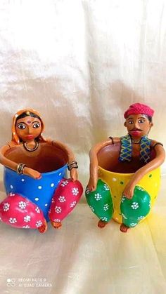 two figurines sitting on top of each other holding pots with flowers in them