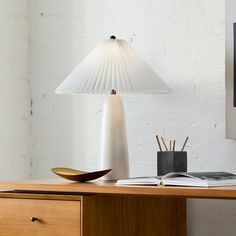 a white lamp sitting on top of a wooden desk next to a book and pen