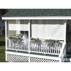 a small white house with green roofing and plants on the porch area next to it