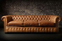 a brown leather couch sitting in front of a brick wall