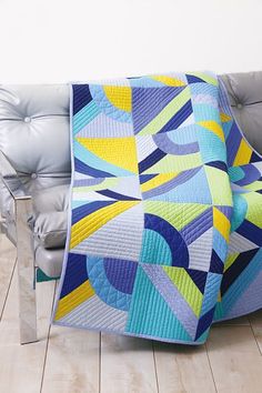 a blue and yellow quilt sitting on top of a gray couch next to a white chair