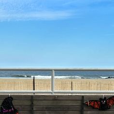 two people sitting on a bench looking at the ocean with kites flying in the air