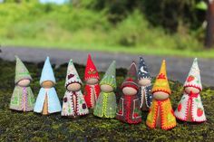 small knitted gnomes are lined up on the mossy ground in front of a road