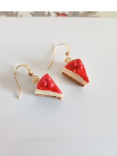 a pair of red and white cheesecake earrings with gold ear wires on a white surface