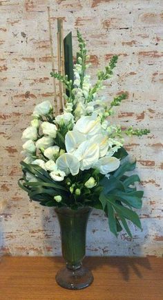 a vase filled with white flowers sitting on top of a wooden table next to a brick wall