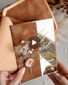 a person holding up a brown and gold wedding card with flowers on the inside of it