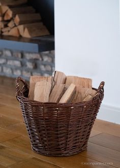 a basket filled with wood sitting on top of a wooden floor next to a fireplace