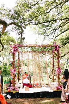 a man and woman sitting at a table in the middle of a forest with flowers on it