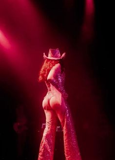 a woman wearing a cowboy hat standing on top of a stage with her legs spread out