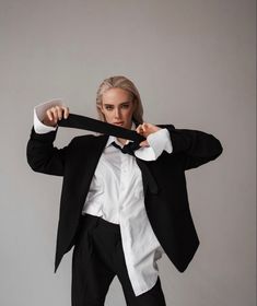 a woman in a tuxedo is holding on to her tie while posing for the camera