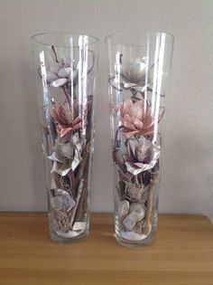 two clear vases with flowers in them sitting on a wooden table next to each other