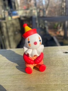 a small toy clown sitting on top of a wooden table next to a building in the background