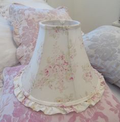 a pink and white lamp shade sitting on top of a bed next to two pillows